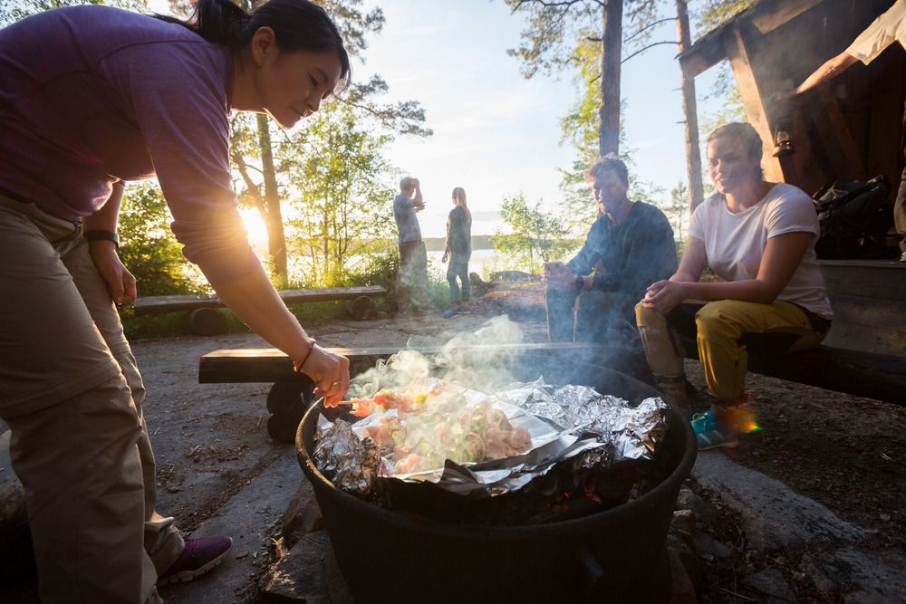 Woman cooking Food over a campfire With Friends In Background