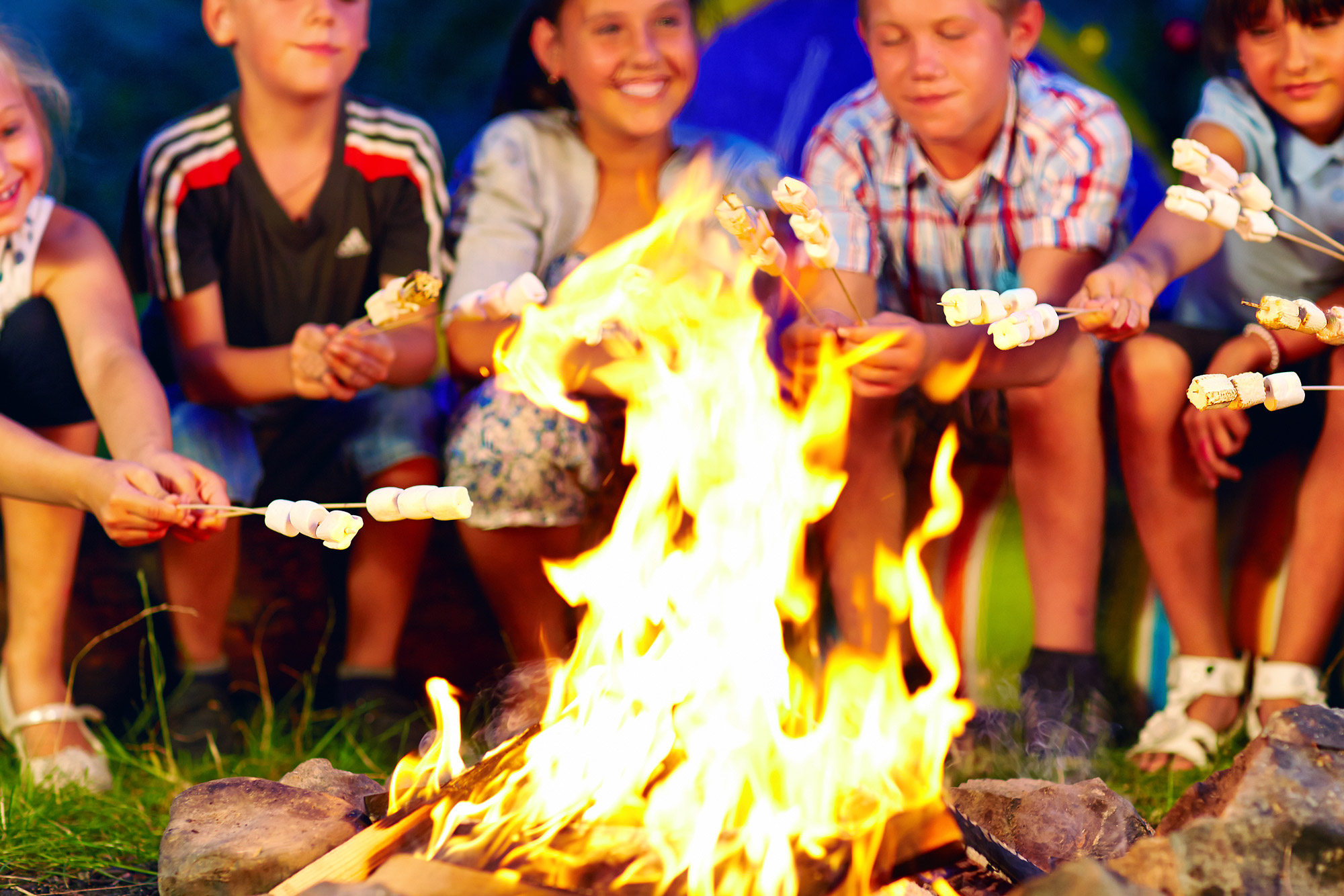 Kids roast marshmallows over a fire. This blog is about campfire desserts that go beyond just s'mores