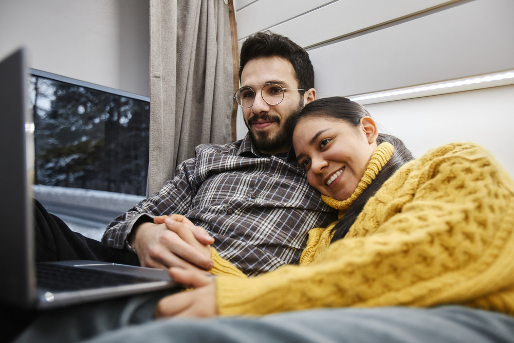 young couple using computer on bed together while travelling in an RV
