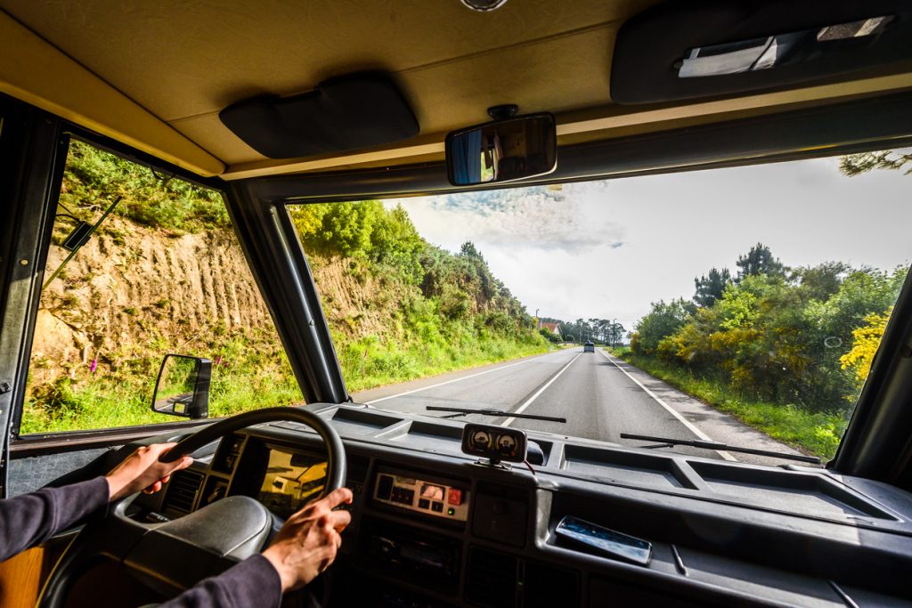 The Best RVs for Tall People: A man's hands on the wheel of a tall RV driving down the road.