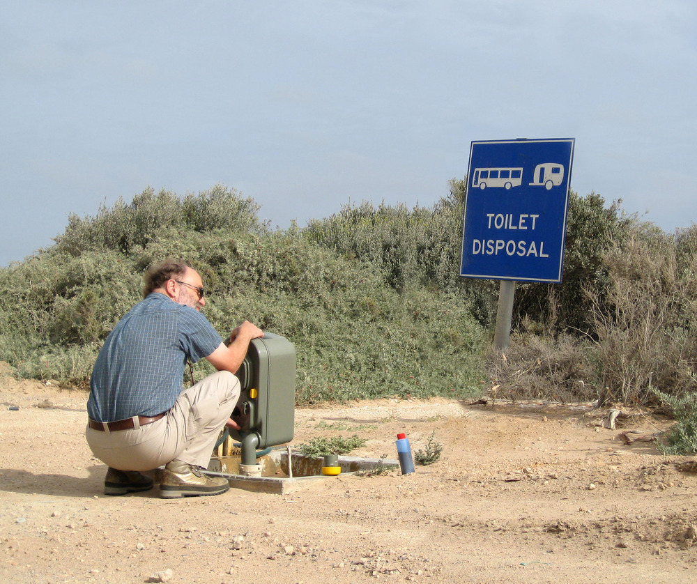 man kneeled down emptying his RV black water tank at a dumping station from his toilet cassette