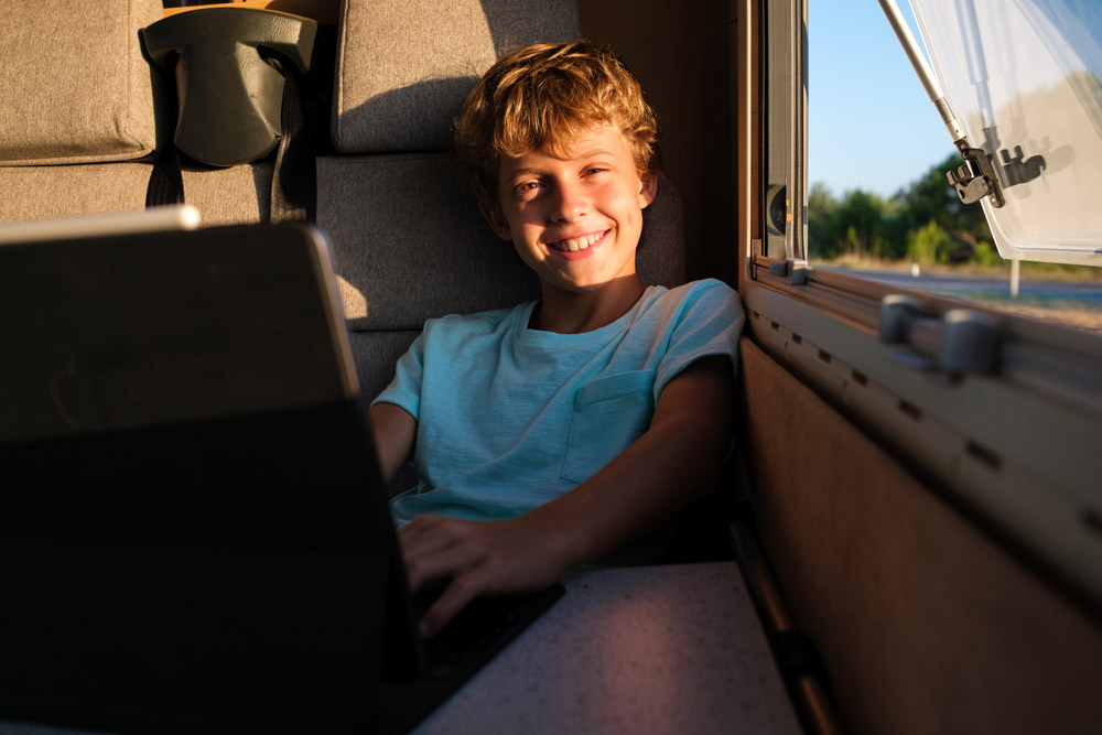 A boy works on his computer for roadschooling inside his family RV