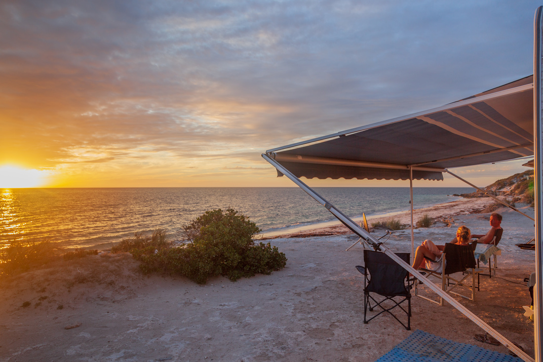 Retired couple sitting under the RV awning enjoying a wine next the beach with a golden sunset.