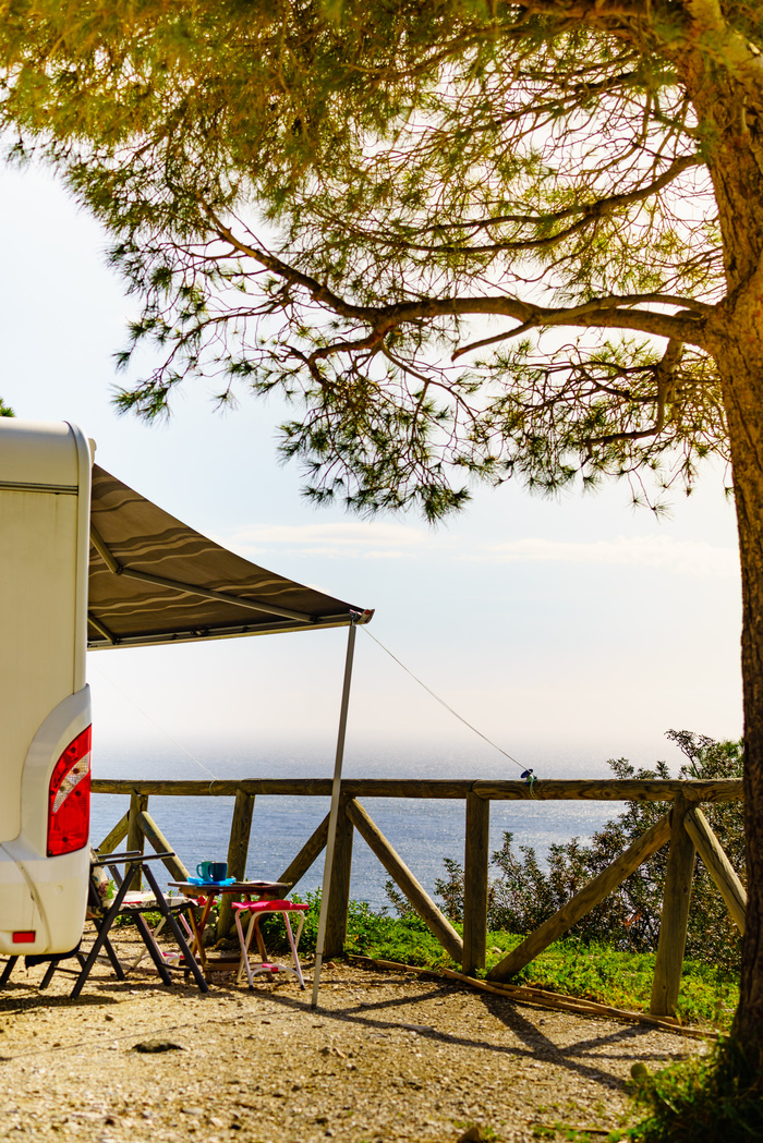 Camper vehicle with roll out awning and tourist table with chairs on the coast.