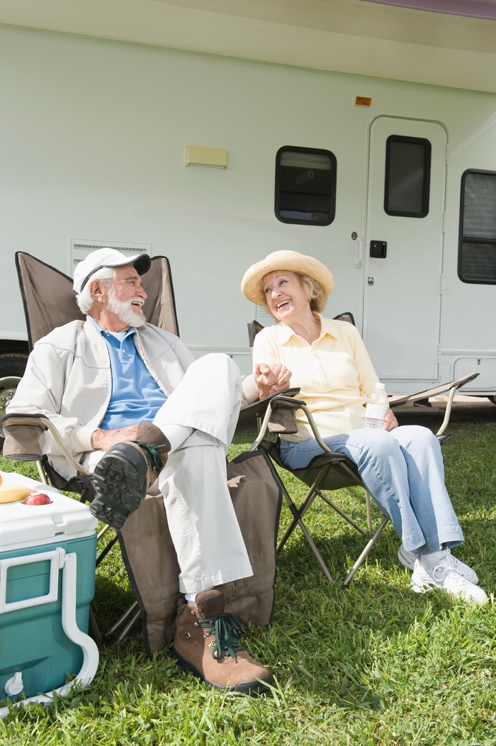 Full length of happy senior couple sitting on folding chairs outside RV home