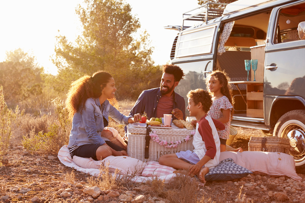 A family has a picnic outside of their camper van on a summer day.