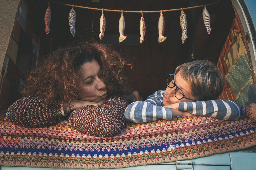 A mom and son sit in the back of a camper van