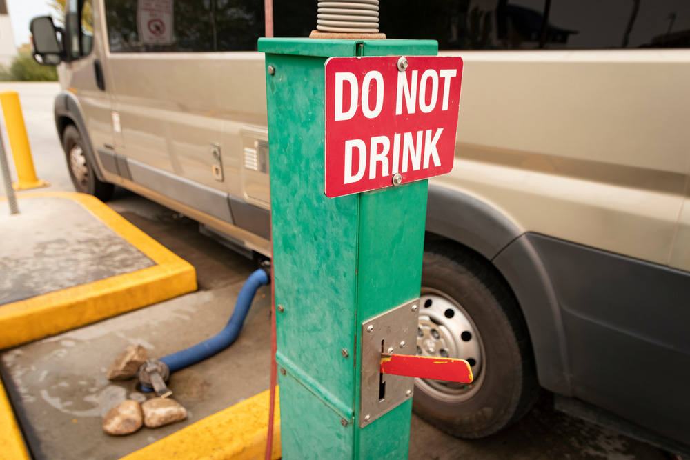 RV emptying its RV black water tank at a dumping station next to a "DO NOT DRINK" sign. 