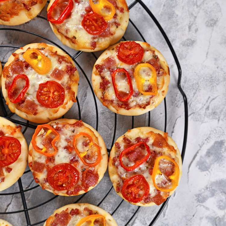 Top view of small mini pizzas topped with cheese, tomato, yellow and red bell peppers and salami sausage