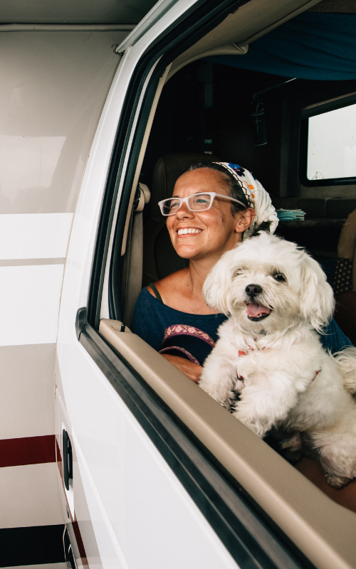 Women holding her little white dog sitting in the passenger seat of an RV on the way to camp.