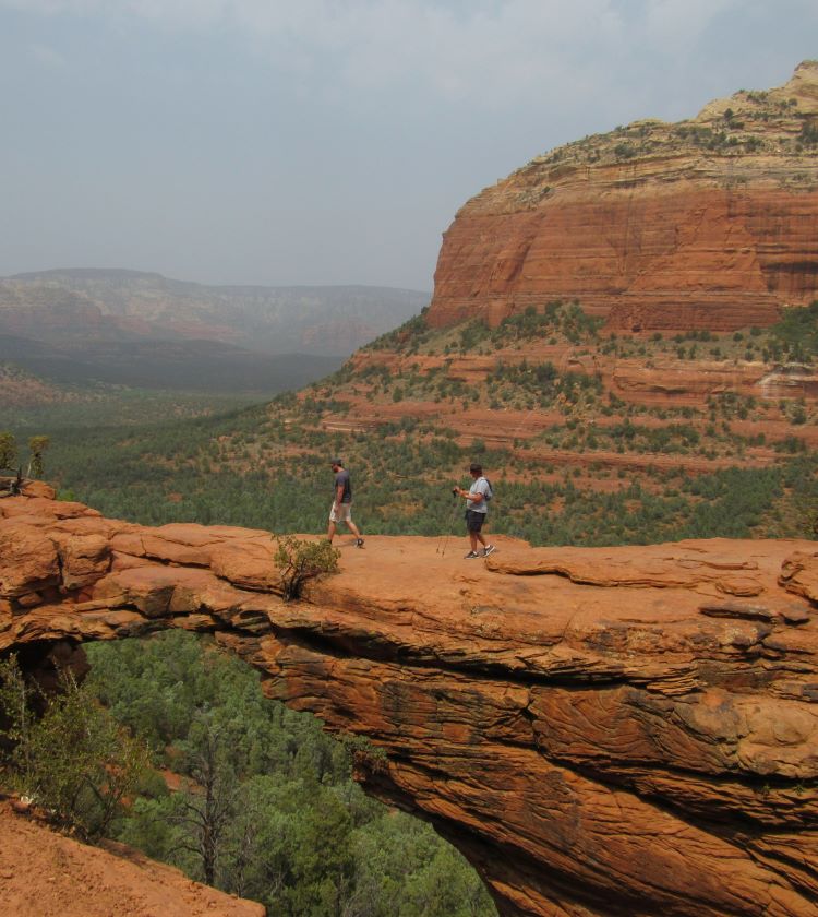 people on Devil's Bridge, the natural arch formation, with red rock mountains in the background located in Sedona, Arizona