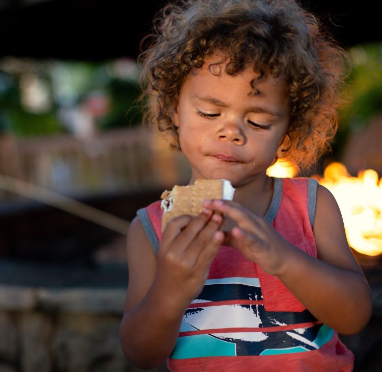 eating smores while rving with kids little boy about to eat a s`more while sitting by an outdoor fire while RVing with family