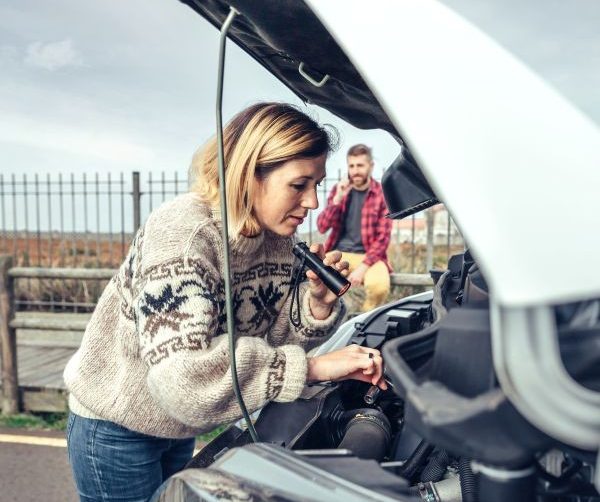 Woman repairing broken down campervan while her husband calls on the phone