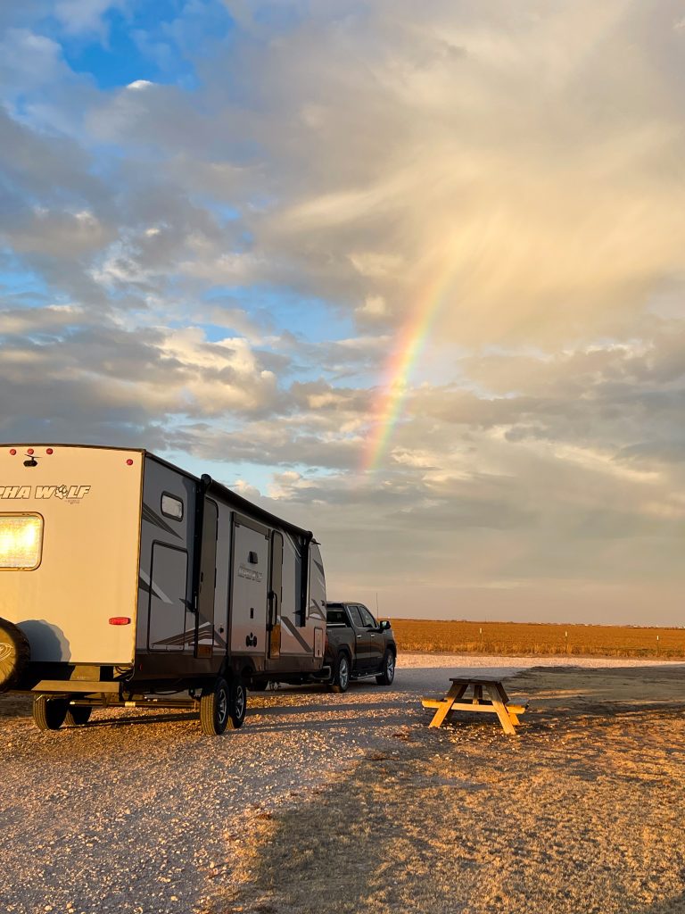 Jon and Carol's truck and travel trailer on a gravel road with a rainbow in the background. 