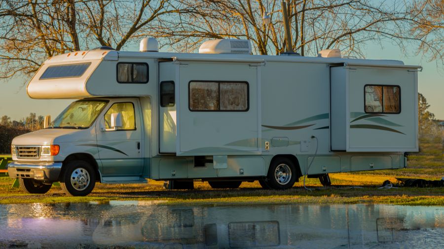 Rv class C motorhome with slides out parked camping next to water early morning light
