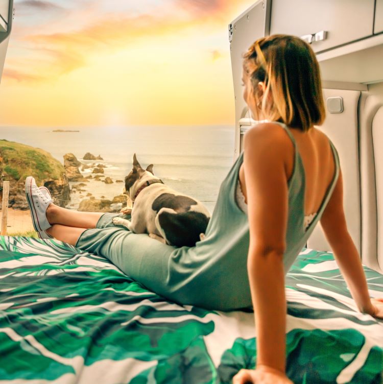 Unrecognizable young woman with her boston terrier dog watching the sunset sitting on the bed of her RV