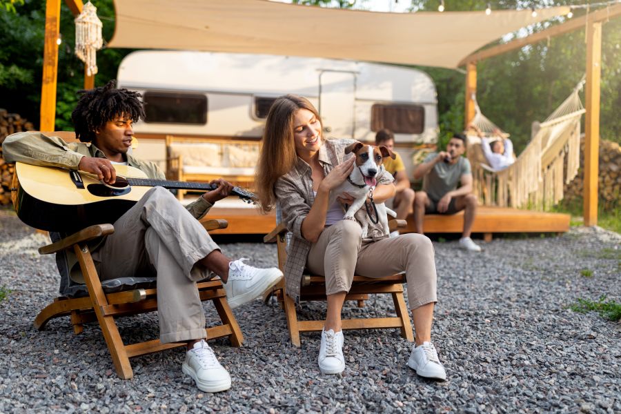 Young guy playing guitar and singing, lady holding dog near RV