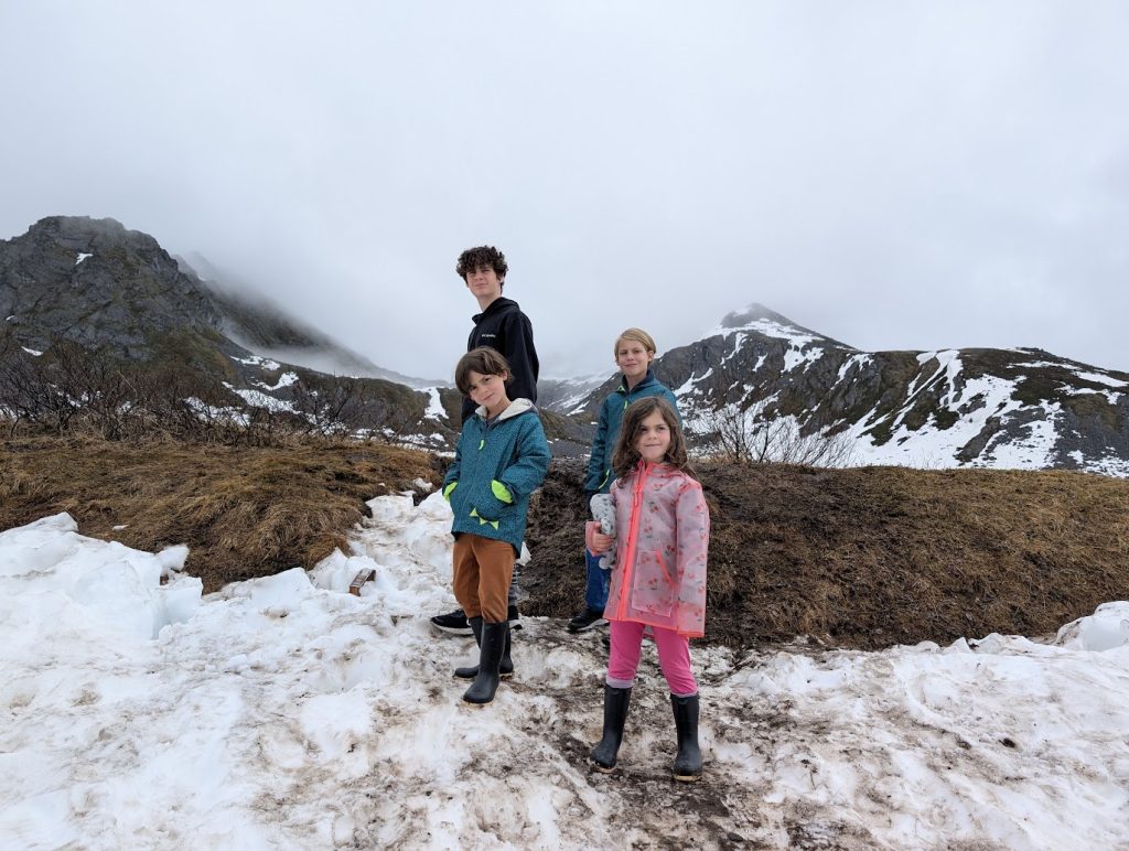 All four Shik children in the snow smiling at the camera on an RV trip.