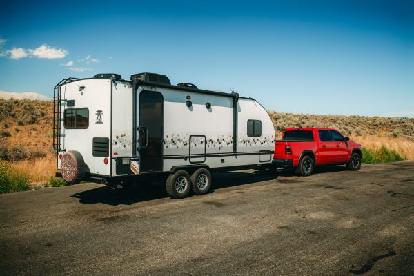 Red pickup truck towing travel trailer on desert roadside under clear blue sky