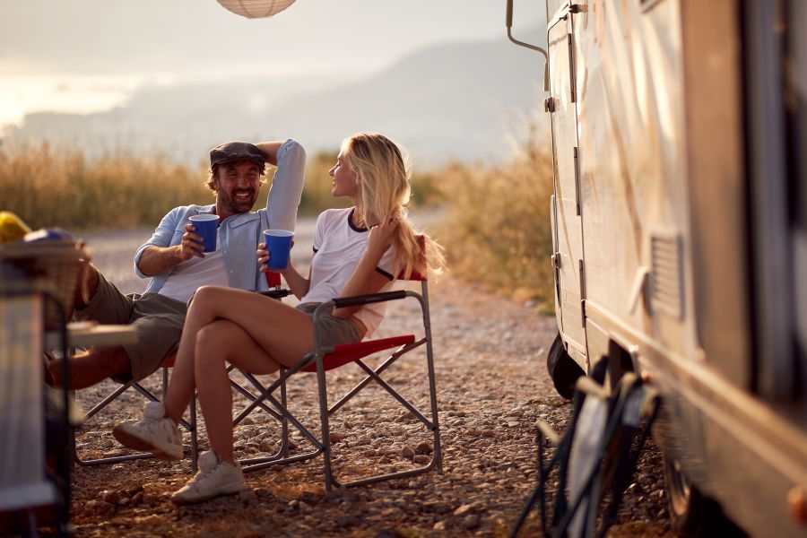 Couple at sunset cheering with drinks. Sitting in front of camper rv.