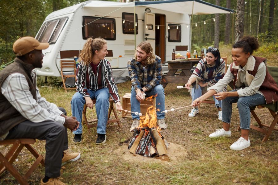 group of young people roasting marshmallows while enjoying camping with friends in forest